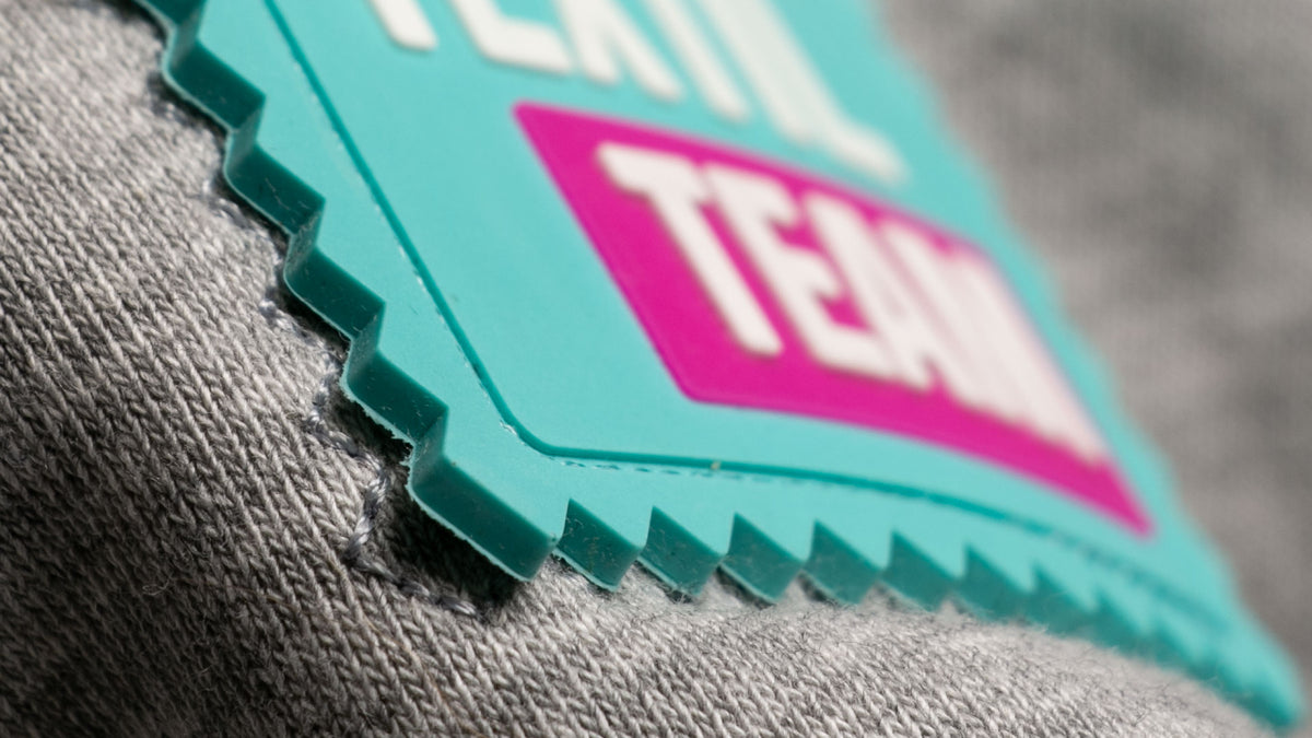 TEXTIL.Team Logo-Patch auf grauem Stoff – veredelbare Basic-Textilien